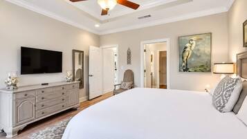 Spacious, elegant bedroom with TV, tray ceiling, and serene decor