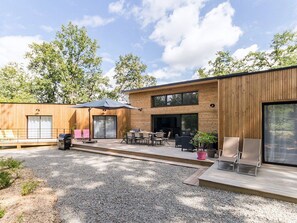 Ein modernes, zweistöckiges Haus mit einer Terrasse, die Gartenmöbel und einen Grillplatz bietet.