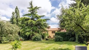 A garden with a table and chairs, surrounded by trees and a building. - Charming Farmhouse Near Nantes with Pond, WiFi, and Baby Equipment (Corcoué-sur-Logne)