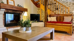 A cozy living room with a fireplace, two TVs, a wooden bench with cushions, and a stone wall.