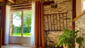 A room with stone walls, a wooden ceiling, a large window with curtains, and a potted plant.