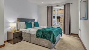 A bedroom with a bed, nightstand, lamp, and a view of the outside through a window. - Chic 2 Bed Apartment in Shoreditch Square (London)