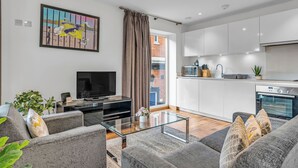 A modern living room with a flat-screen TV, grey sofas, and a glass coffee table. - Chic 2 Bed Apartment in Shoreditch Square (London)
