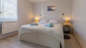 A bedroom with a bed, bedside lamps, a window with curtains, a radiator, and a picture on the wall. - Modern Coastal Home with Garden, Terrace & Parking Near Beaches - Pornic (Pornic)