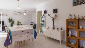 A modern dining area with a table set for two, a white cabinet with shelves, and a painting on the wall. - Modern Coastal Home with Garden, Terrace & Parking Near Beaches - Pornic (Pornic)