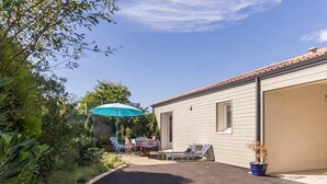 A residential property with a paved driveway, a patio with a table and chairs, and a blue umbrella. - Modern Coastal Home with Garden, Terrace & Parking Near Beaches - Pornic (Pornic)
