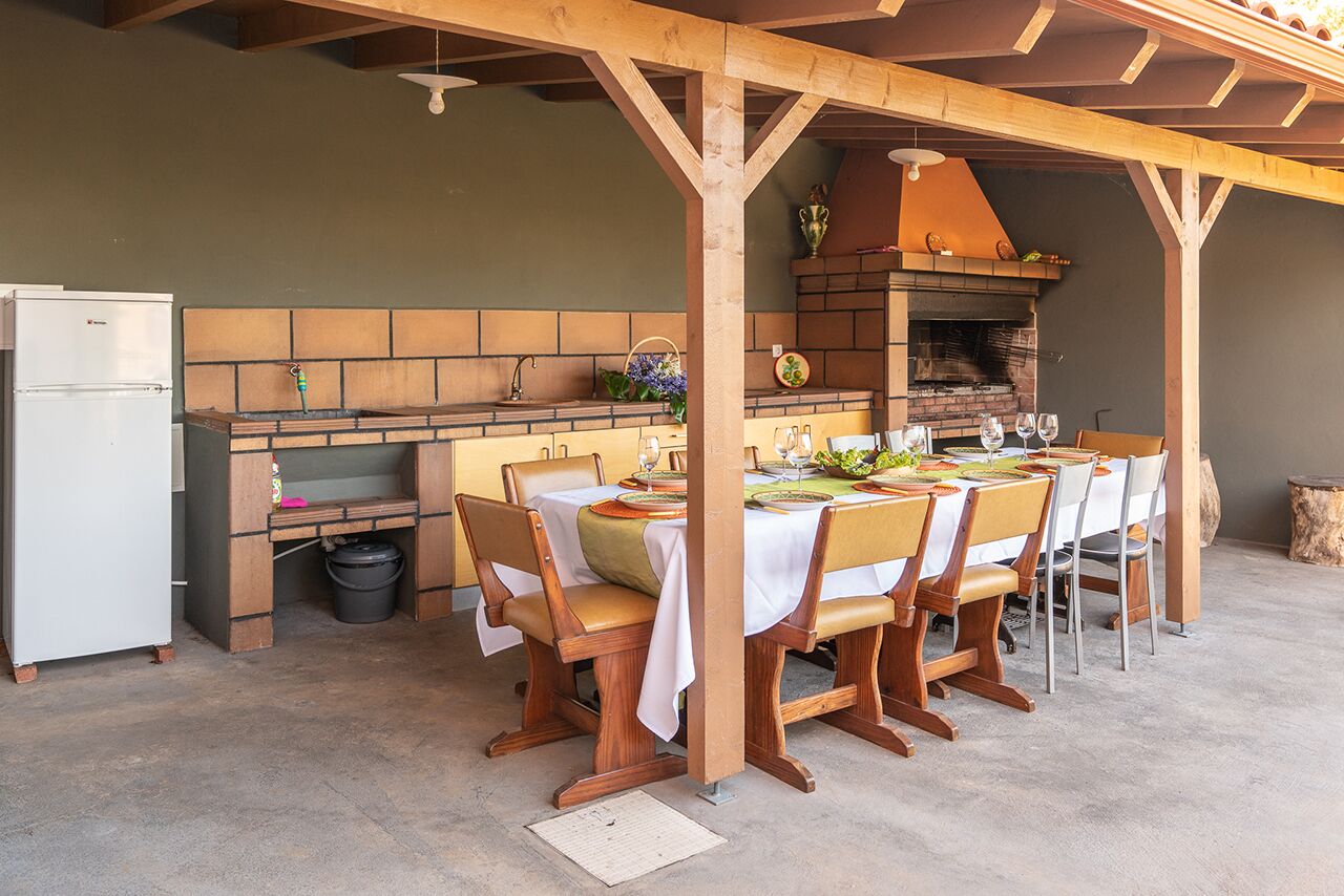 Een buiten eethoek met een bakstenen muur, houten stoelen, een tafel gedekt voor vier personen en een pizzaoven.