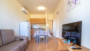 Ett kompakt bostadsutrymme med en soffa, ett matbord med stolar, en tv och ett köksområde med skåp och ett kylskåp.