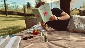 Une personne est assise sur une couverture à l’extérieur et lit un livre.