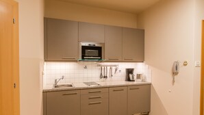 Une cuisine compacte avec des meubles gris, un four en acier inoxydable, une machine à café et un téléphone fixé au mur.