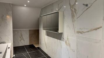 Un baño moderno con pared de mármol, ducha integrada y espejo.