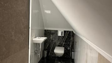 Een compacte, smalle badkamer met een witte wastafel, toilet en een marmeren spatwand.