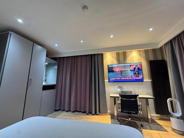 A hotel room with a bed, a television mounted on the wall, a desk with a chair, and a sound system.