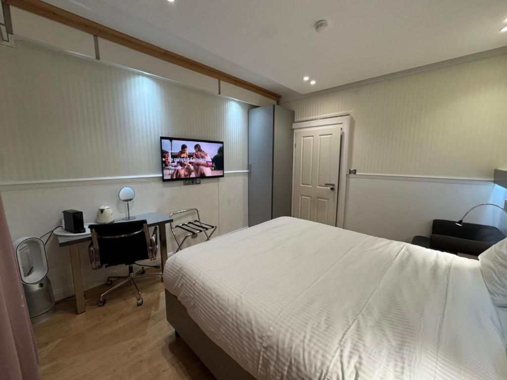 Une chambre d’hôtel comprenant un lit, un bureau avec un ordinateur, une chaise, un téléviseur fixé au mur et une porte.