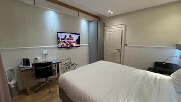 Een hotelkamer met een bed, een bureau met een computer, een stoel, een aan de muur bevestigde televisie en een deur.