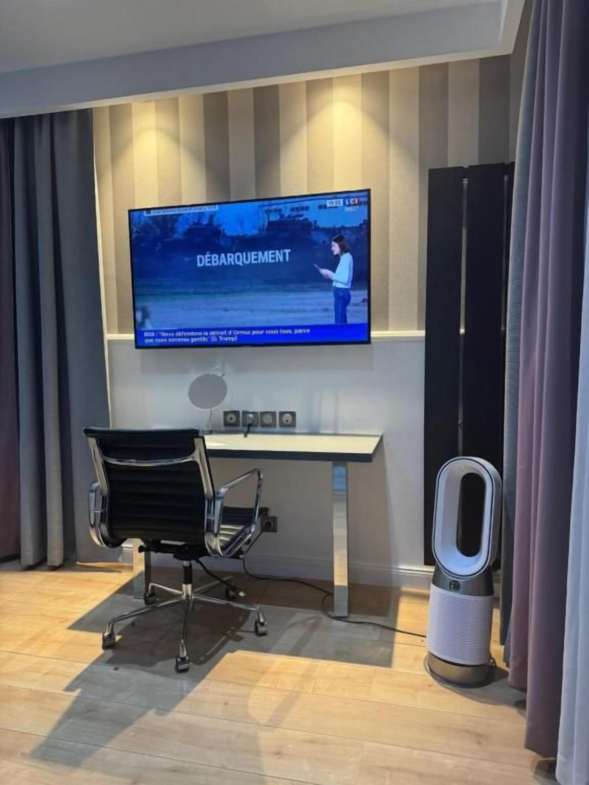 Una habitación moderna con una televisión de pantalla plana montada en la pared, un escritorio con una silla y un calentador portátil.