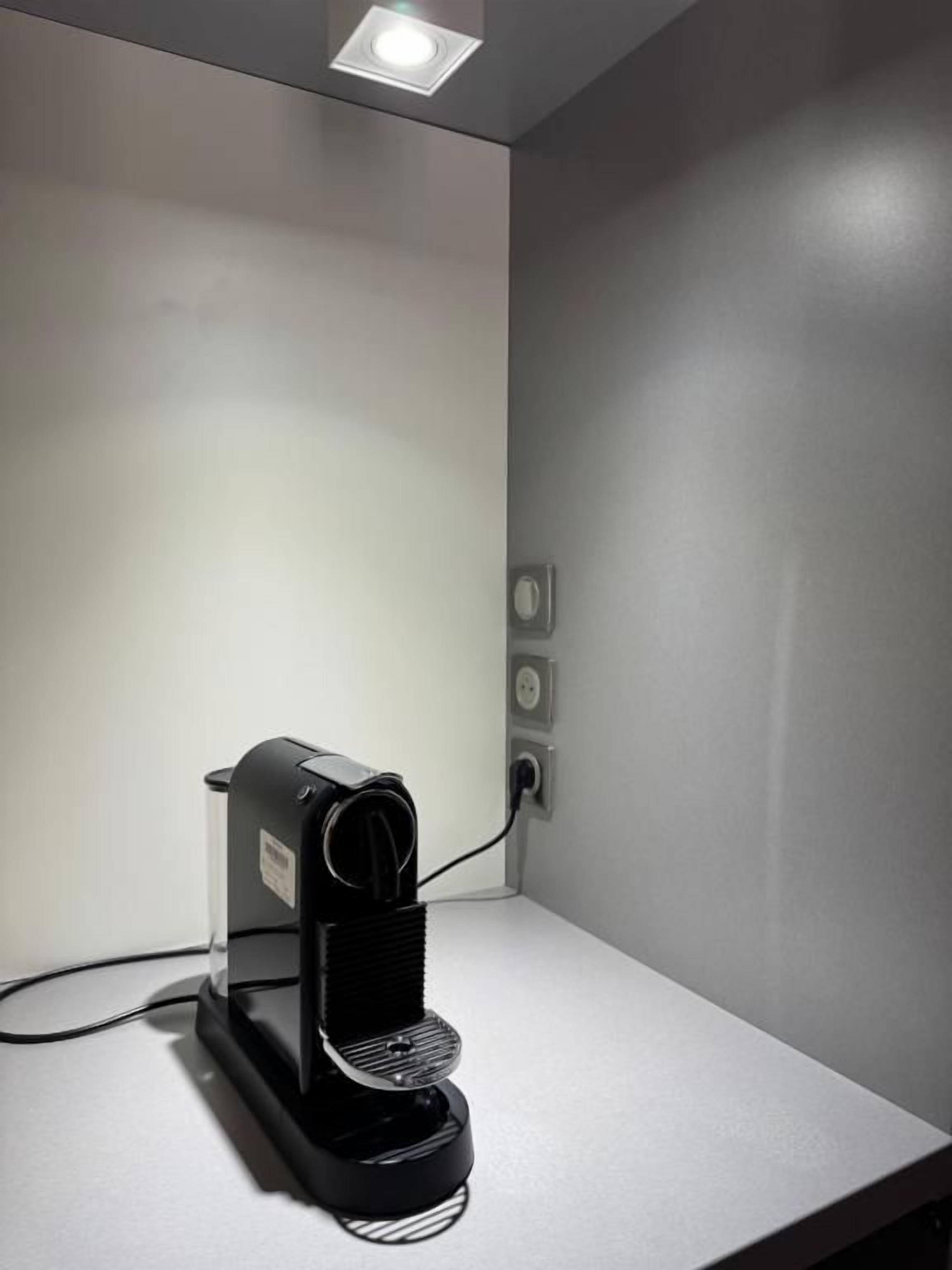 A coffee machine on a white countertop with a wall-mounted electrical outlet nearby.