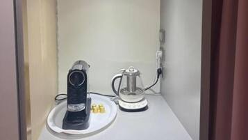 Un petit espace clos comprenant une machine à café et une bouilloire, le tout posé sur un plan de travail blanc.