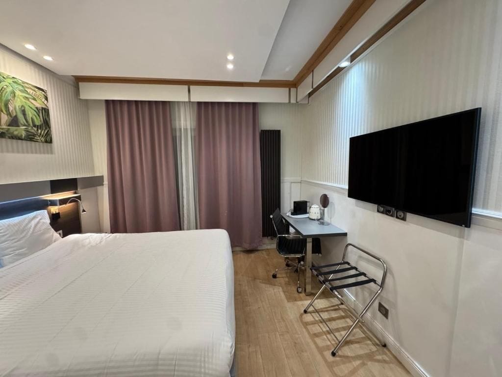 Habitación de hotel con cama, escritorio, silla y televisor montado en la pared.