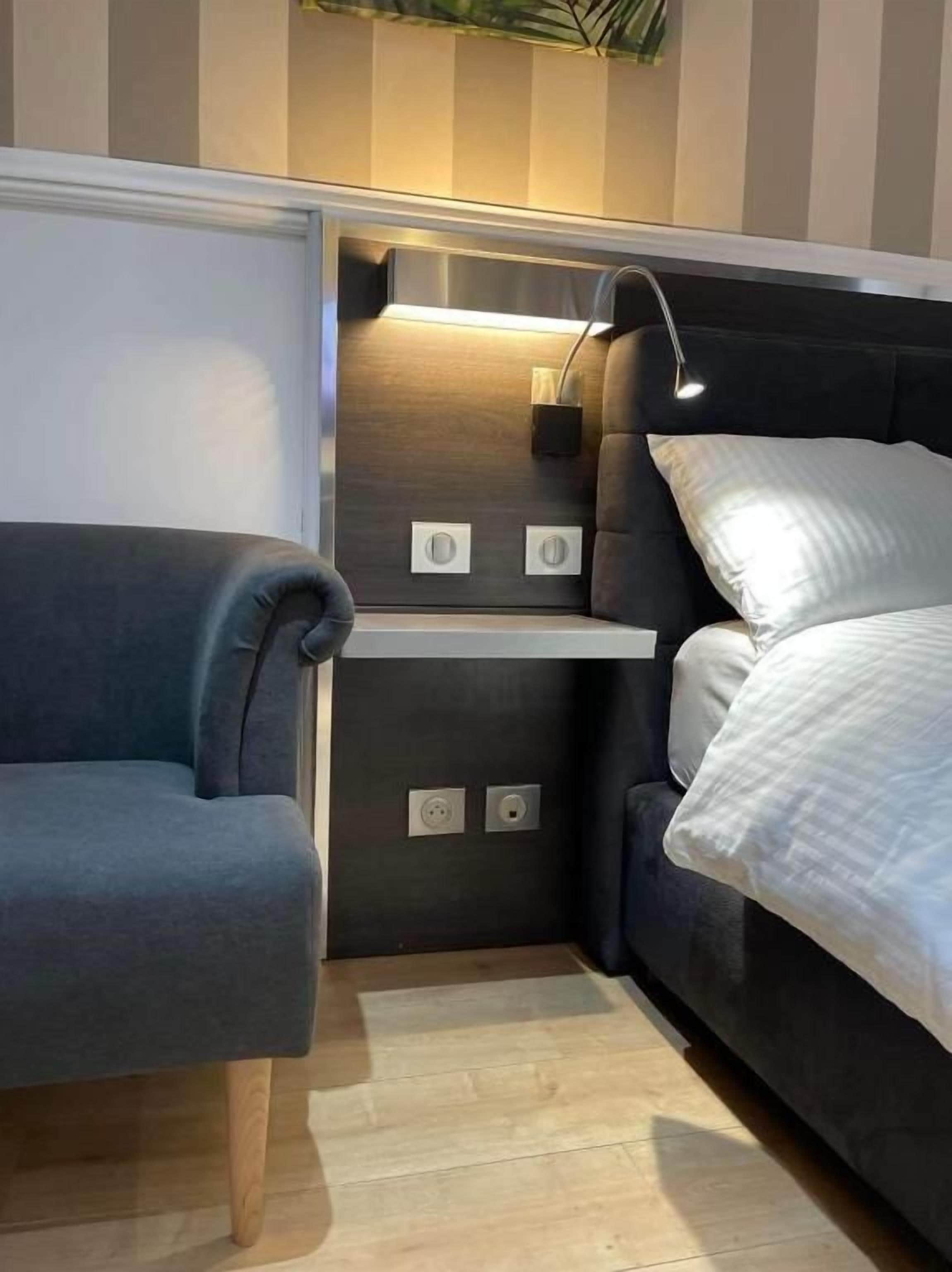 Una habitación compacta con cama, un pequeño rincón de descanso y estantería empotrada.