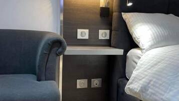 Una habitación compacta con cama, un pequeño rincón de descanso y estantería empotrada.