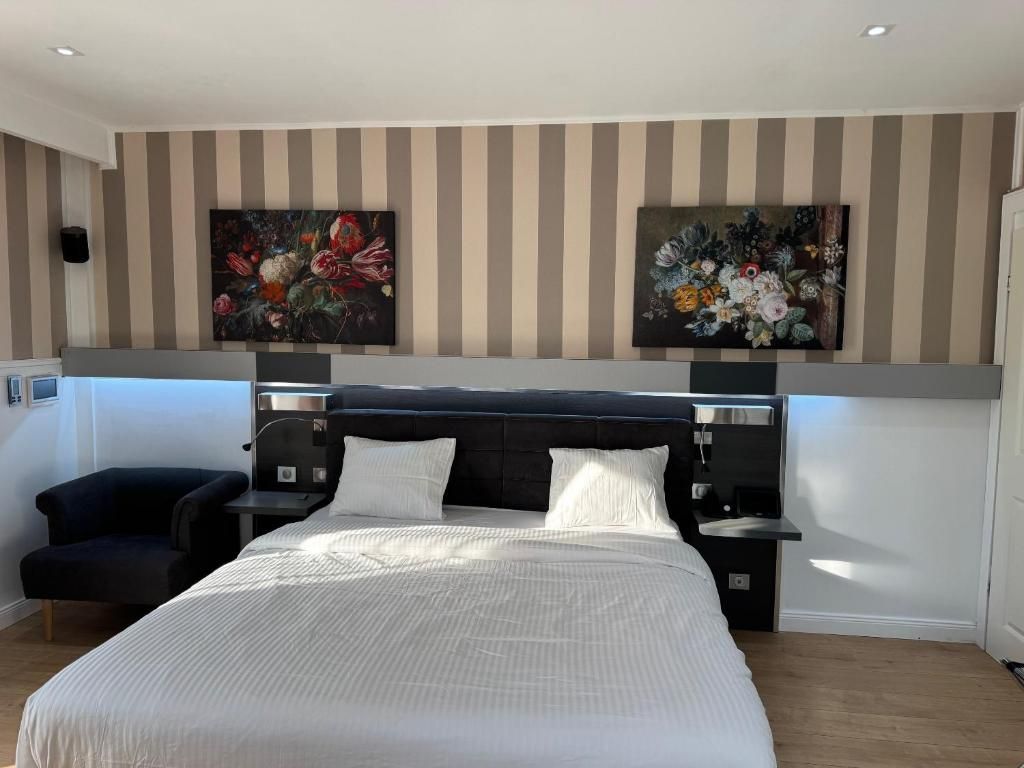 A hotel room with a large bed, a bedside table, a chair, and two wall-mounted paintings.