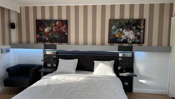 A hotel room with a large bed, a bedside table, a chair, and two wall-mounted paintings.