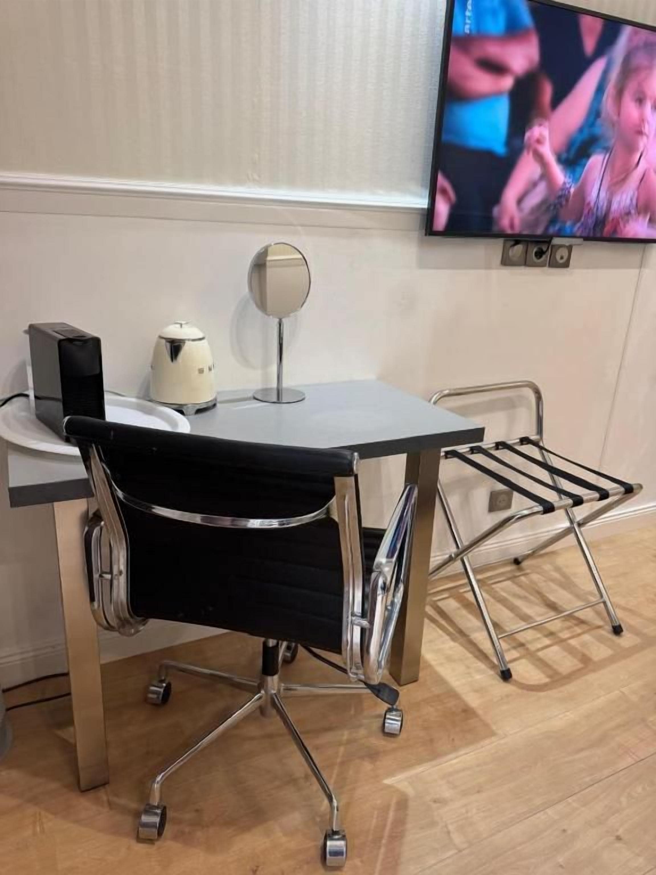Un fauteuil de bureau moderne sur roulettes, un téléviseur à écran plat fixé au mur et une petite table avec une bouilloire et un haut-parleur.