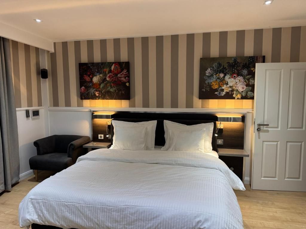 A hotel room with a large bed, a chair, a nightstand, and two wall-mounted paintings.