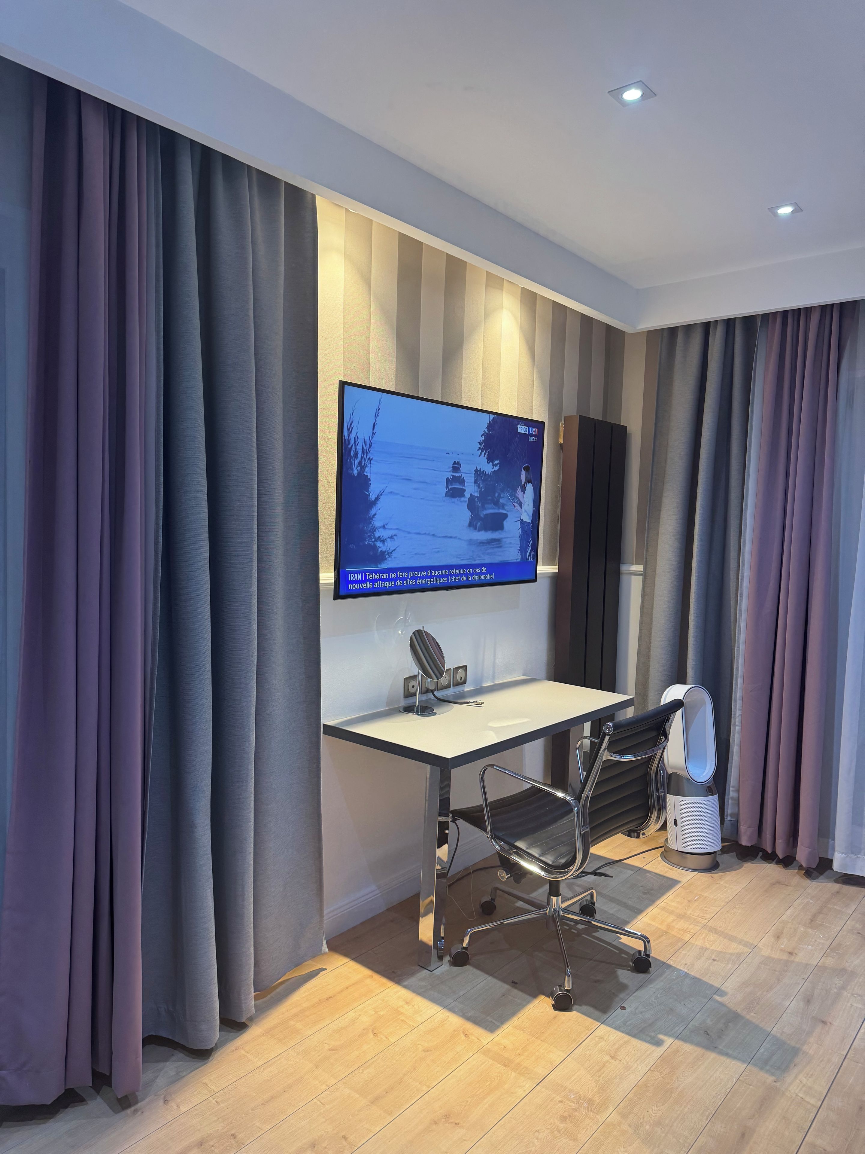 Een moderne kantoorruimte met een grote flatscreen televisie aan de muur, een bureau met stoel en een speaker.
