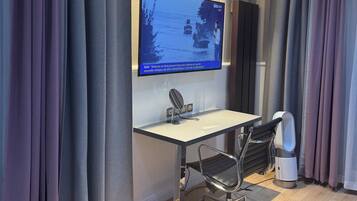 Een moderne kantoorruimte met een grote flatscreen televisie aan de muur, een bureau met stoel en een speaker.