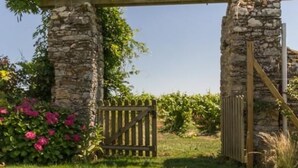 Une porte en pierre surmontée d’une clôture en bois, le tout entouré d’une végétation luxuriante et de plantes en fleurs.