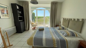 Une chambre à coucher avec un lit, une chaise, un téléviseur, un radiateur et une vue sur l’extérieur.