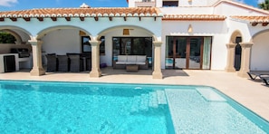 A poolside area with a clear pool, outdoor seating, and a covered patio with arches.