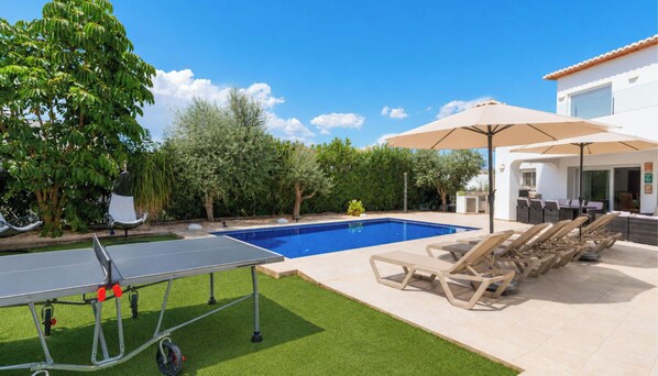 A poolside area with a table tennis table, lounge chairs, and a covered seating area.