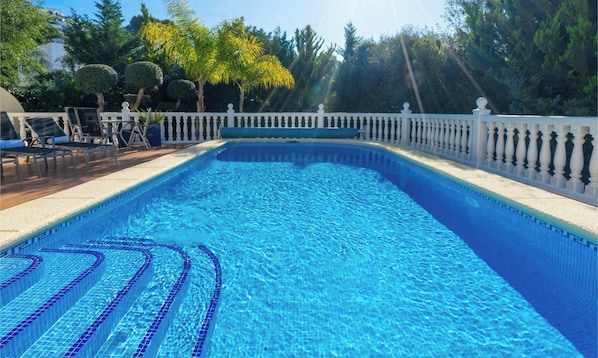 Una piscina con recinzione bianca, sdraio e alberi sullo sfondo.