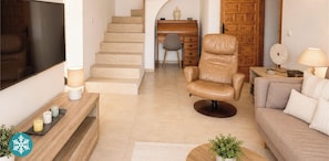 A living room with a leather armchair, a sofa, a TV, a desk with a chair, and a staircase.