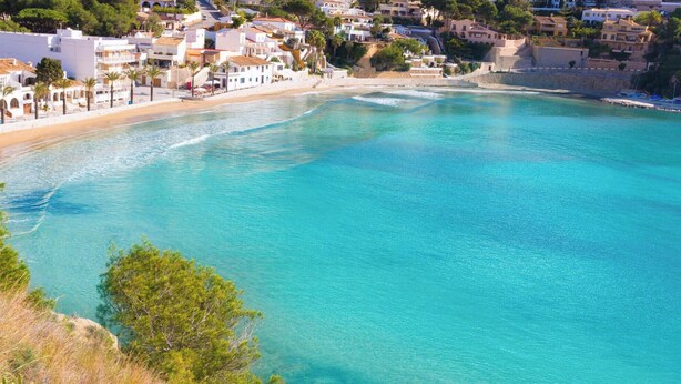 Une ville côtière dotée d’une plage, d’eaux turquoise et limpides, et de bâtiments blancs.