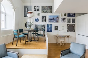 Un comedor moderno con una mesa y sillas de madera, una pared blanca con obras enmarcadas, y un ventanal que proporciona luz natural.