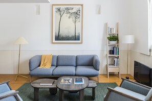 Olohuone, jossa on harmaa sohva, kirjoja sisältävä sohvapöytä, kirjahylly ja televisio.
