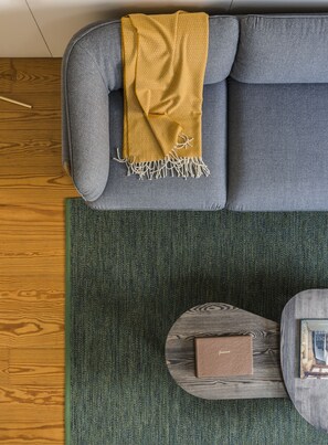 A grey sofa with a mustard-colored throw blanket, a green textured rug, and a wooden coffee table with a book. - Flattered to be in Porto City View Apartment B (Oporto)
