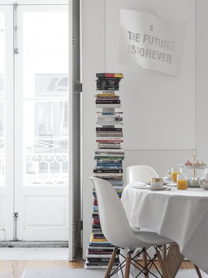 Una habitación con una pila de libros en una pared blanca, una mesa con mantel blanco y un cartel que dice 'THE FUTURE IS FOREVER'.