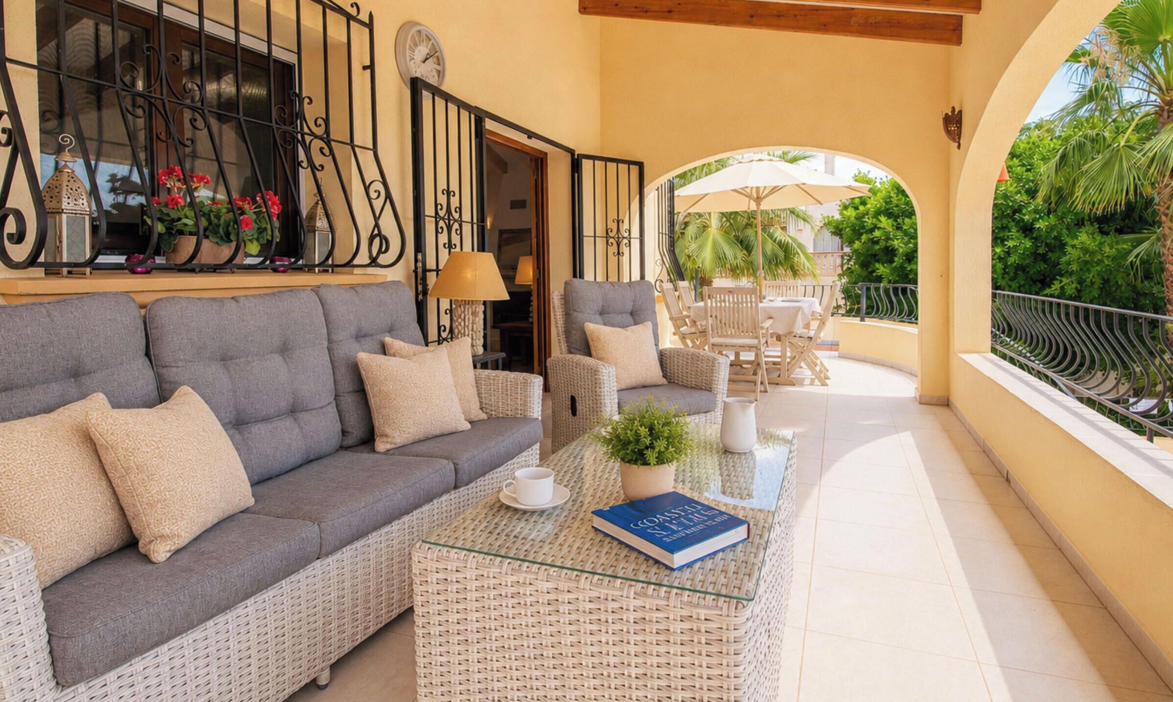 A balcony with a grey sofa, wicker coffee table, and outdoor furniture.