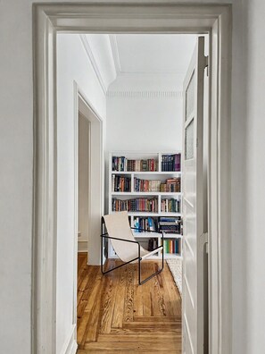 A hallway leading to a room with a bookshelf, a chair, and wooden flooring. - Flattered to be in Lisboa N (Lisboa ciudad)