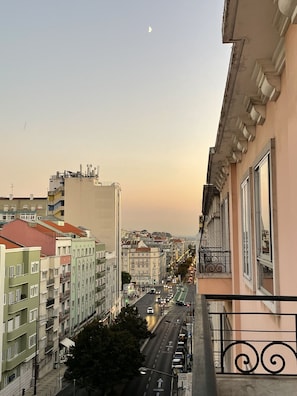 Una calle urbana con edificios, cielo despejado y una luna creciente.