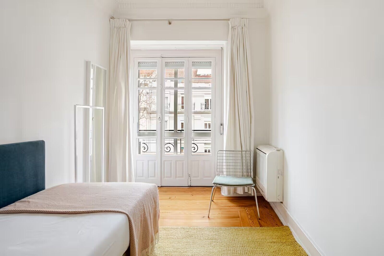 Un dormitorio con cama, una silla, un radiador y vistas a través de una puerta.