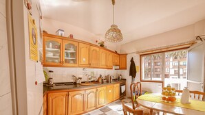 A kitchen with wooden cabinets, a checkered floor, a dining table with chairs, and a view of buildings outside. - Aguere Nest Hostel (San Cristóbal de La Laguna)