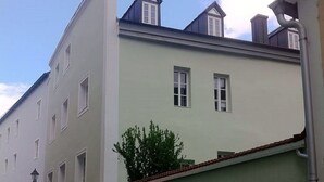Una calle estrecha flanqueada por edificios, con un camino empedrado y un pequeño árbol frente a uno de ellos.