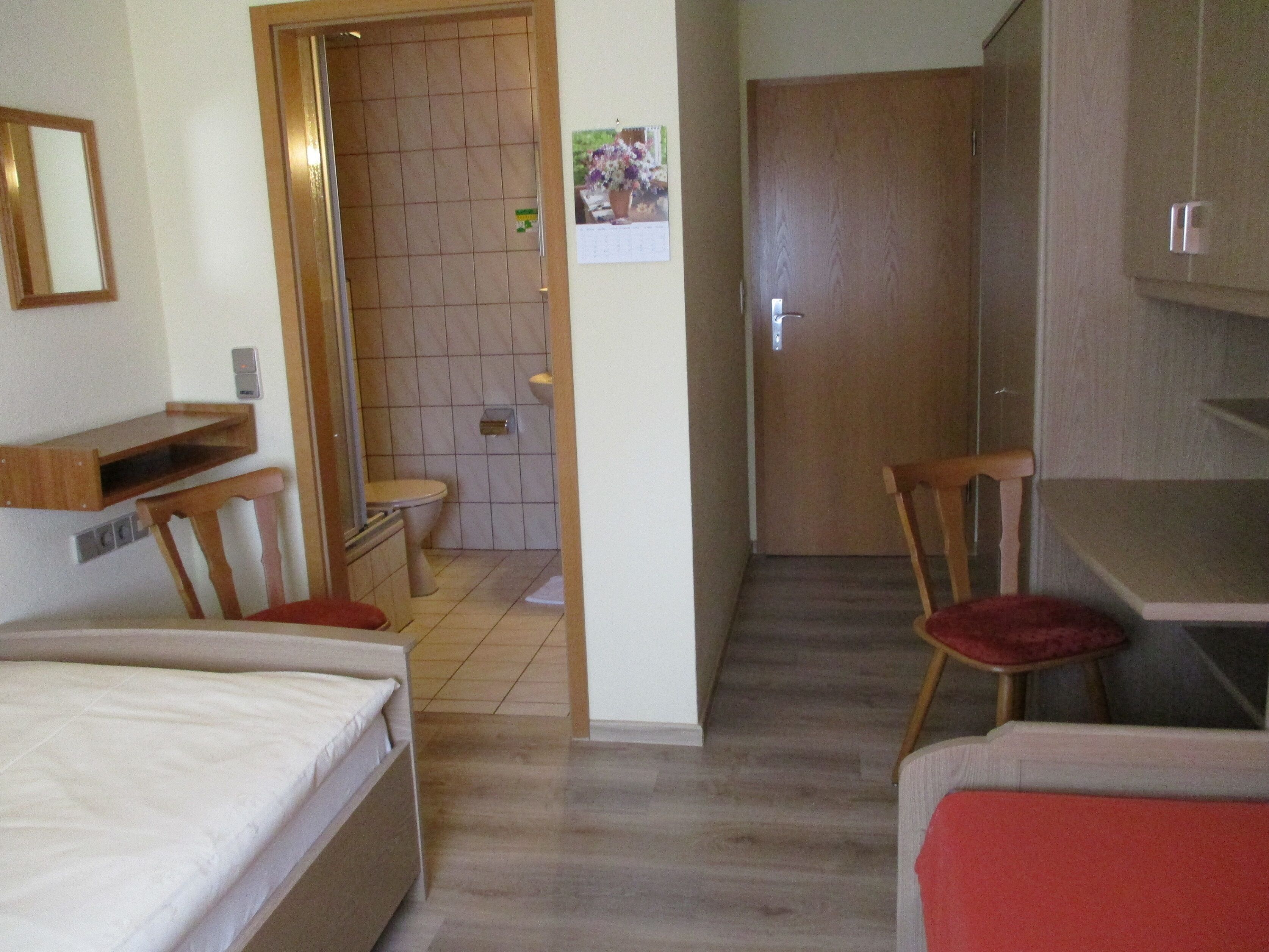 A compact hotel room with a bed, a desk, a chair, a small bathroom, and a wooden door.