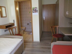 A compact hotel room with a bed, a desk, a chair, a small bathroom, and a wooden door.